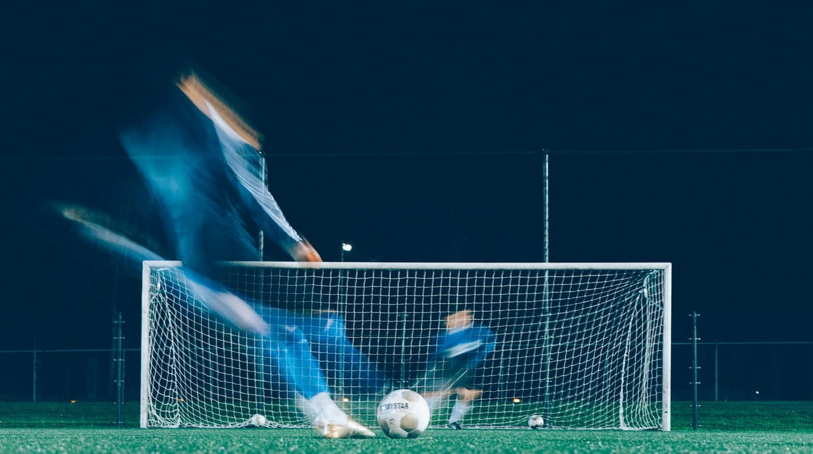 Voetballer in beweging voor het doel op een verlicht veld bij avond