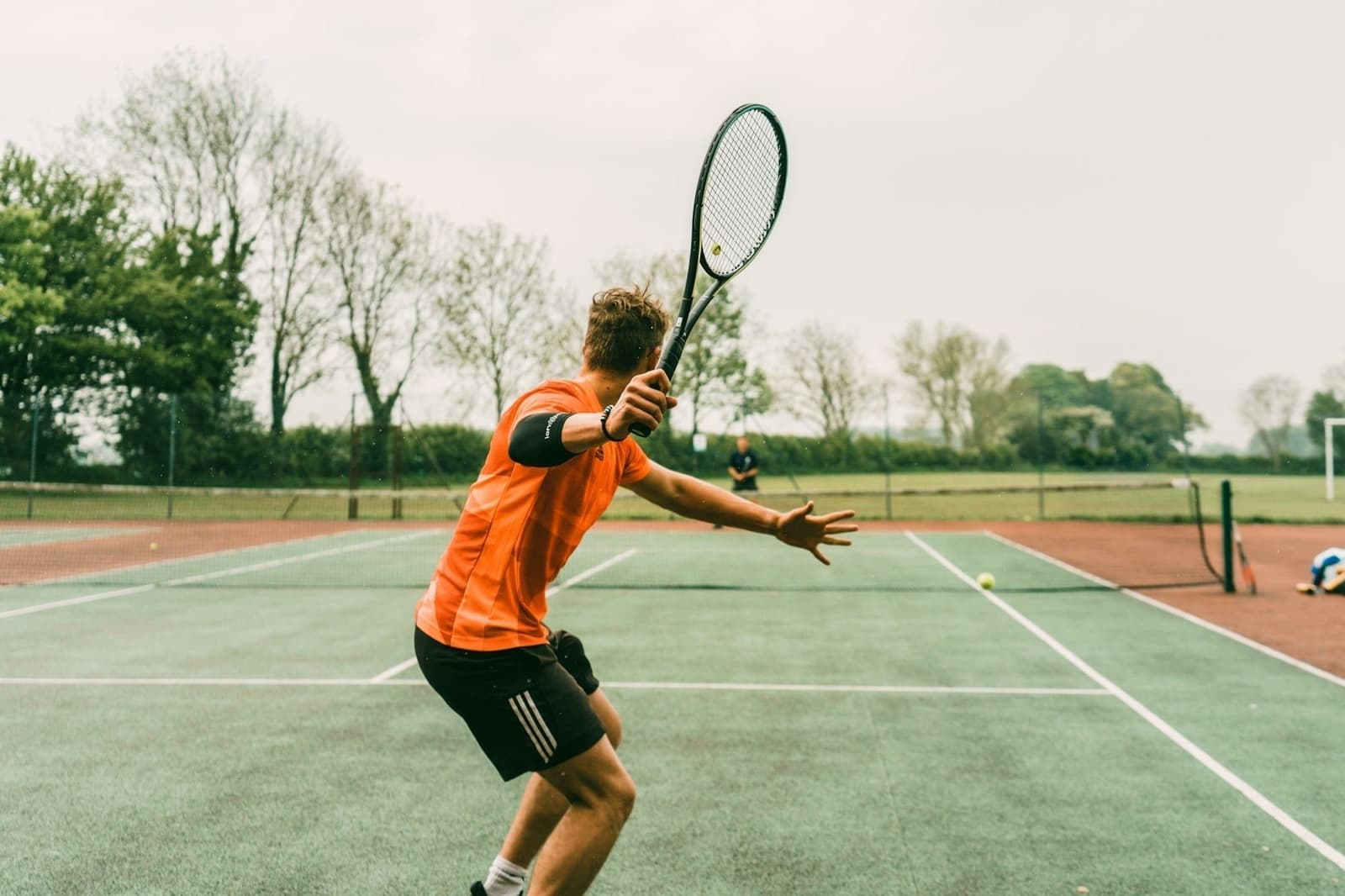 Tennisser in oranje shirt maakt een slag op een buitenbaan