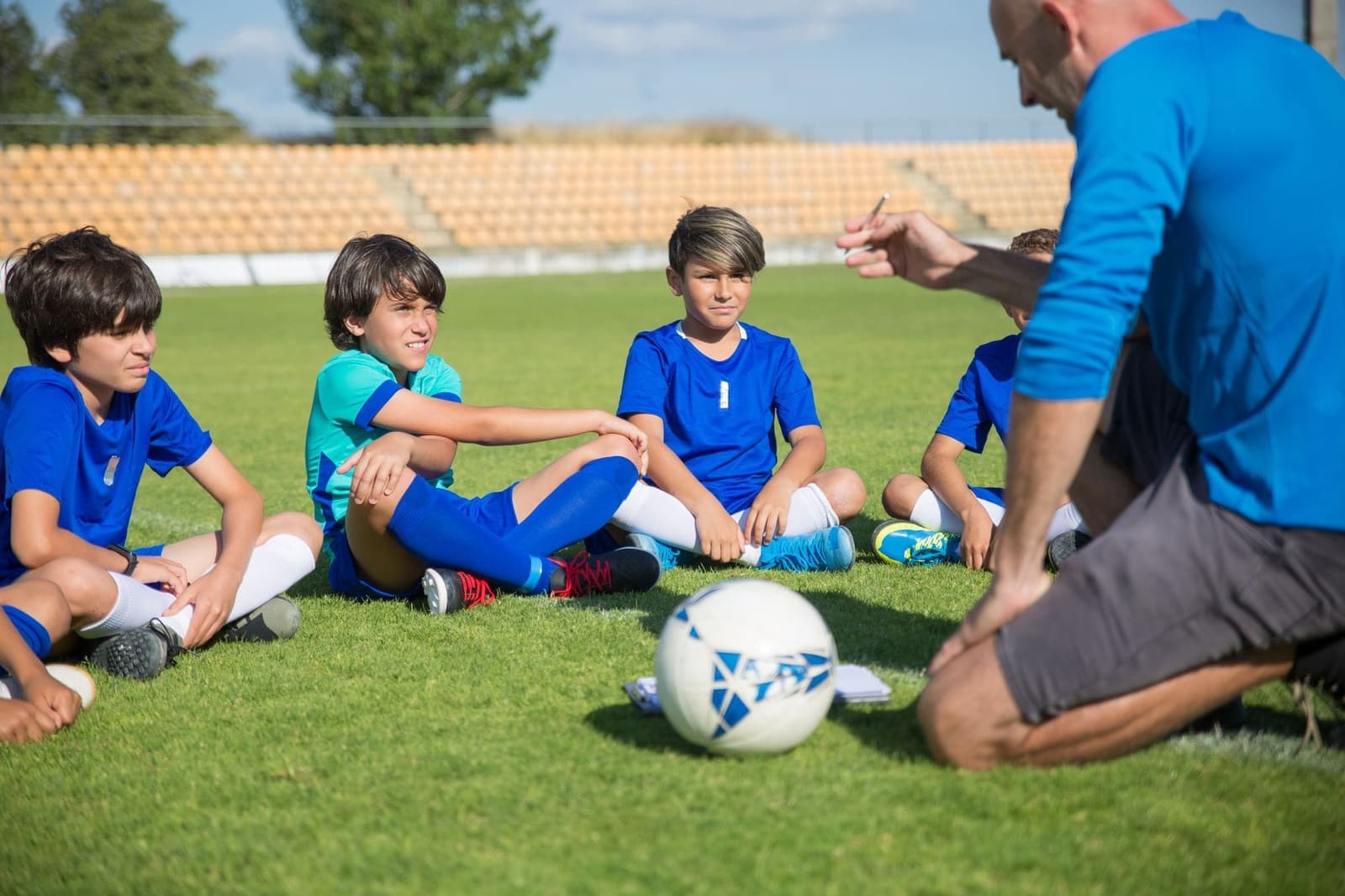 Jeugdvoetballers zitten op het gras en luisteren naar hun trainer