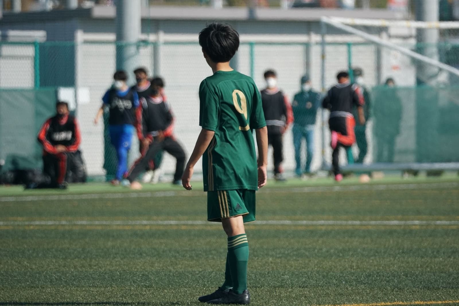 Jonge voetballer in groen tenue met nummer 9, van achteren gezien op het veld