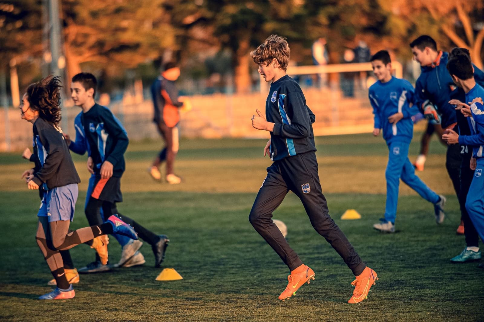 Jeugdvoetballers op training in het avondlicht, met pionnen op het veld