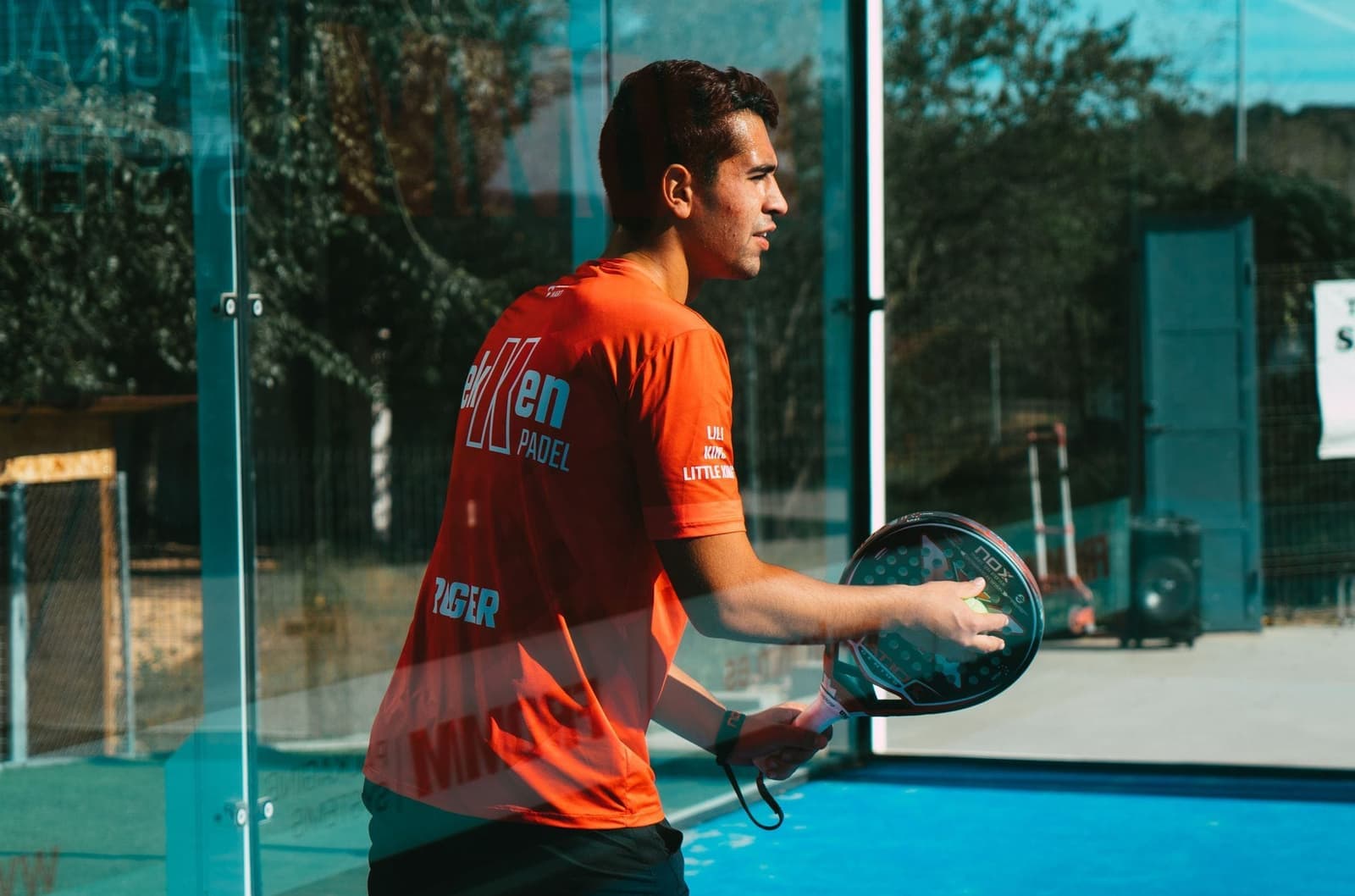 Padelspeler in oranje shirt in een glazen padelkooi